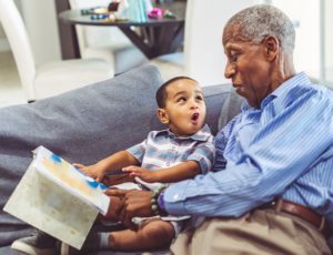 Adorable toddler with his grandfather at home reading a book together