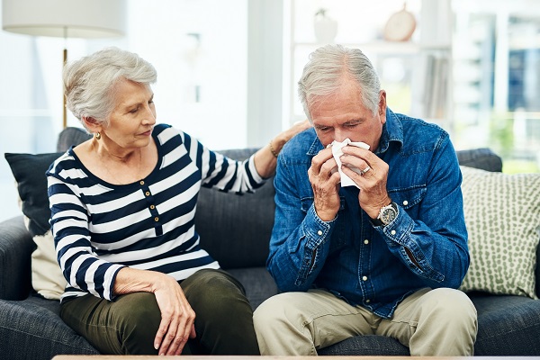 Shot of a senior man blowing his nose with his wife comforting him on the sofa